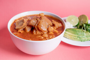 Exquisite Mexican Menudo on a white plate accompanied by a dish with condiments on the back.