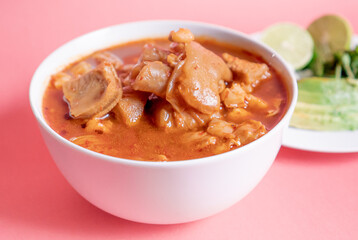 Exquisite Mexican Menudo on a white plate accompanied by a dish with condiments on the back.