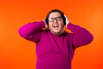 Fototapeta premium Relaxed funny thick man, dances while listens music, moves arms and closes eyes in enjoyment, wears headphones on ears, has fun and feels aspiration.