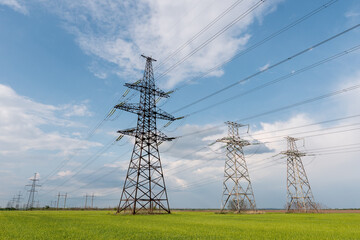 High voltage lines and power pylons and a green agricultural landscape on a sunny day.
