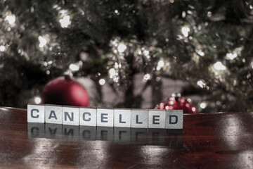 Wooden letters spelling CANCELLED due to COVID-19 restrictions with a christmas tree in the background. Selective Focus.