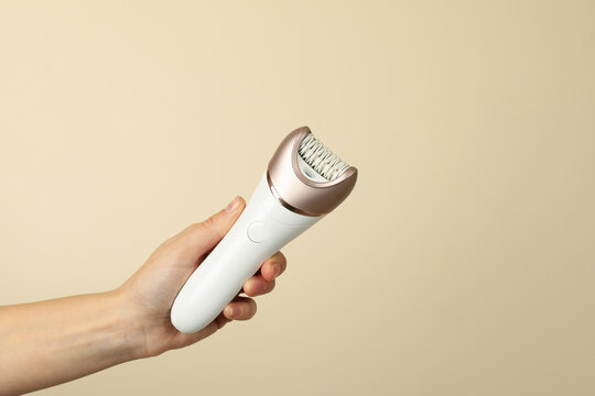 Female hand hold epilator on beige background, space for text