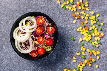 Top view of the healthy colorful salad bowl with tomatoes fresh mixed leaves vegetable in a dish on cement stone table background, Health salad snack diet food weight loss concept