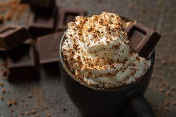 Hot chocolate  cup with whipped cream  and chocolate slices  on dark concrete background. Warm cozy...