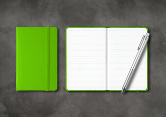 Green closed and open lined notebooks with a pen on dark concrete background
