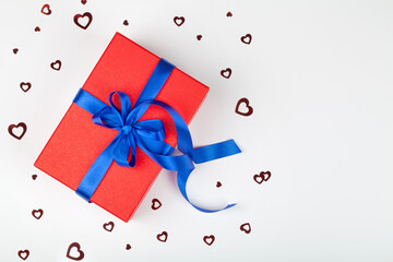 red gift or present box with blue ribbon and heart confetti on white background.