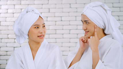 Two Asian girls in white bathrobes with towels on heads talking in living room.