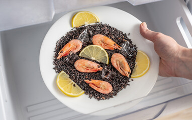 Women's hands are taking out a plate of black rice, shrimps and lemon from the freezer of the fridge. Concept of ready made frozen dishes