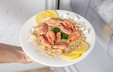 Women's hands are taking out a plate of rice, shrimps and lemon from the freezer of the fridge. Concept of ready made frozen dishes and saving time on cooking food