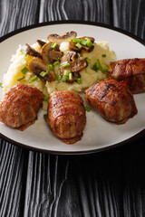 Dutch Slavinken is an excellent comfort food cooked of ground meat wrapped in bacon served with mashed potatoes and mushrooms closeup in the plate. vertical