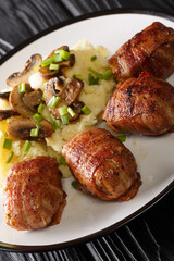 Slavink is a Dutch meat dish consisting of ground meat wrapped in bacon served with mashed potatoes and mushrooms closeup in the plate on the table. vertical
