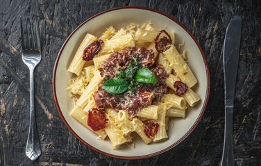 Plate of delicious appetizing vegetarian pasta with tomato sauce, tomatoes, cheese and basil on a black table. Top view
