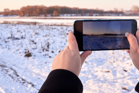 A tourist photographs a snow-covered road and a river on a smartphone in winter.