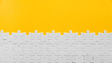 Top view of a white jigsaw puzzle on a yellow background with copy space.