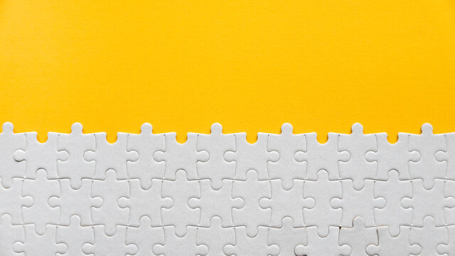 Top view of a white jigsaw puzzle on a yellow background with copy space.
