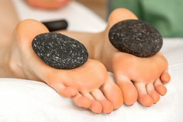 Fototapeta na wymiar Massage stones lying on soles of female bare feet in spa salon