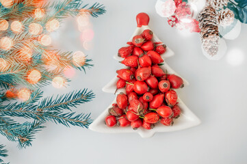 Rosehip berries in a porcelain dish in the shape of a Christmas tree on a light background close-up. Berries for making vitamin tea or drink on cold winter days