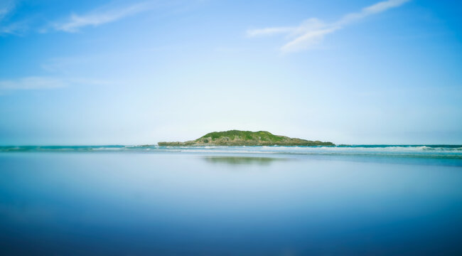 Reflections of Little Muttonbird Island on the leeward side with blue sky background.