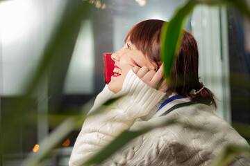 a young pretty girl in a white sweater smiles and talks on the phone at home by the window