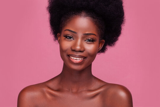Portrait of a gorgeous fashion model African American girl smiling on camera with bare shoulders and afro hair isolated on pink background.