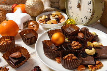 sweet food background for christmas or holiday decoration - chocolate candies, tangerines, nuts and dried fruits on white wood