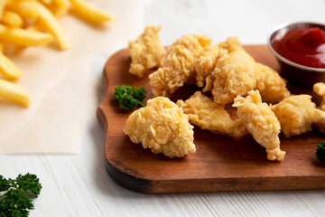 Homemade Popcorn Chicken on a rustic wooden board on a white wooden background, side view. Close-up.