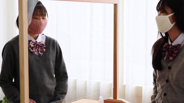 マスクをつけて飛沫防止パーテーション越しに談笑する日本人女子学生