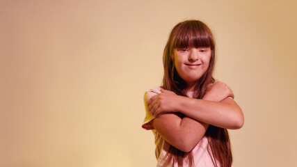 Portrait of disabled girl with Down syndrome smiling at camera, standing with arms crossed while...