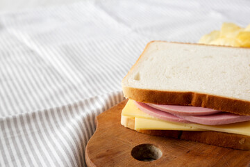 Homemade Bologna and Cheese Sandwich on a rustic wooden board on cloth, side view. Copy space.
