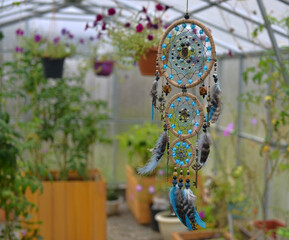 Beautiful handmade boho styled dreamcatcher with feathers and beads against flowers and plants.