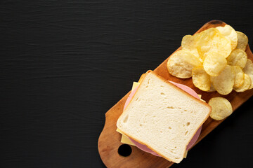 Homemade Bologna and Cheese Sandwich on a rustic wooden board on a black background, top view. Copy space.