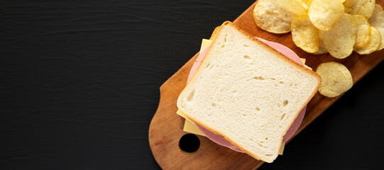Homemade Bologna and Cheese Sandwich on a rustic wooden board on a black background, top view. Copy space.
