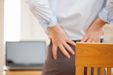 Businessman with backache standing in front of his workplace while working remotely from home