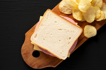 Homemade Bologna and Cheese Sandwich on a rustic wooden board on a black background, overhead view. Flat lay, top view, from above. Copy space.