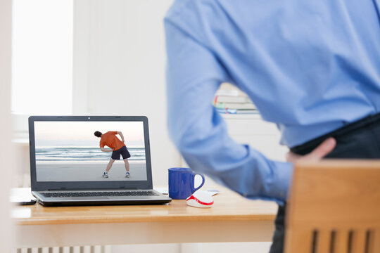 Businessman doing stretching exercise in front of laptop while working from home
