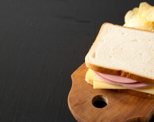 Homemade Bologna and Cheese Sandwich on a rustic wooden board on a black background, side view. Space for text.