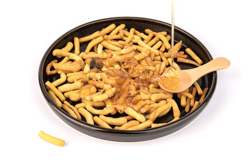 An isolated image of a pile of some bread sticks or cracker sticks on a plate with honey and a spoon on a white plate or table top. Spicy appetizer close-up image on a white background.