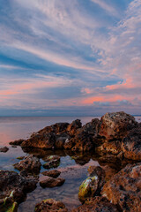 The pink sunset sky is reflected in the sea surface. Rocks and sea.