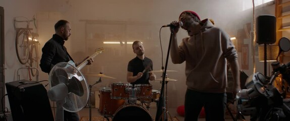 WIDE Friends playing music during their rock band rehearsal repetition inside a garage. Vocals, guitars and drums. Shot with 2x anamorphic lens - Powered by Adobe