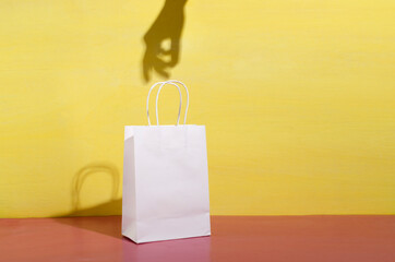 Woman hand shadow on the yellow wall, white shopping bag on the pink surface
