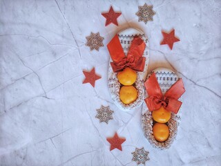 Christmas background of white soft home slippers and red Christmas decoration and orange fresh tangerines. Flat lay, top view. New Years gift ideas.