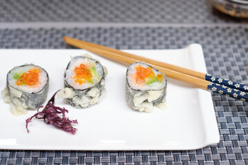 Gunkan Sushi with salmon roe on a white plate with Japanese chopsticks.