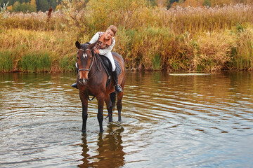 A beautiful girl in a rider's tracksuit is sitting on a horse, they went into the water of the reservoir