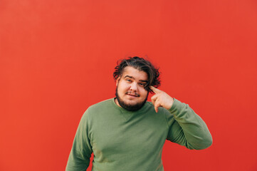 Cheerful obese hispanic young man is pointing a finger at his head, showing a thoughtful gesture,...