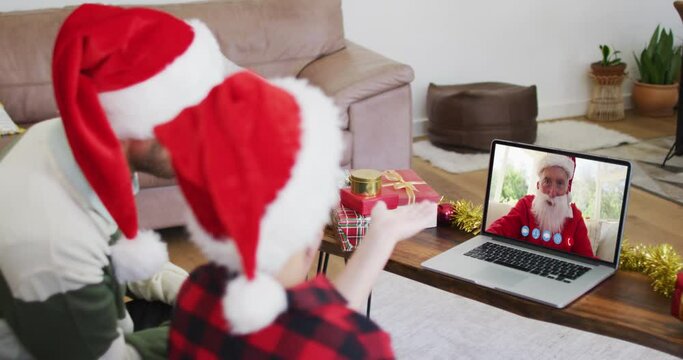 Caucasian man with son wearing santa hats on laptop video chat during christmas at home