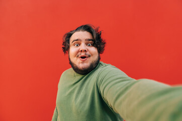 Excited and cheerful hispanic man is taking a selfie on a camera, looking surprised with his mouth...
