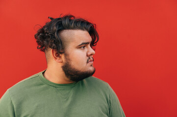 Side view of a handsome bearded hispanic young man, looking serious, posing for a photo on a red...
