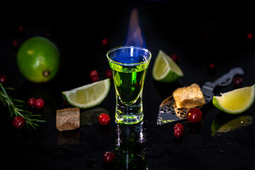 absinthe shots with sugar cubes. absinthe poured into a glass. bottle of absinthe with brown sugar, cranberries and lime, stainless steel spoon isolated on black background. space for text