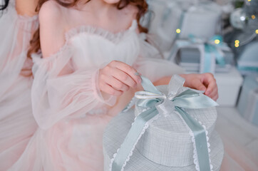 A little girl unties the ribbon on the gift box.
Girl's hands and a gift.