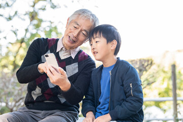 公園で仲良くスマートフォンを見ている孫とおじいちゃん